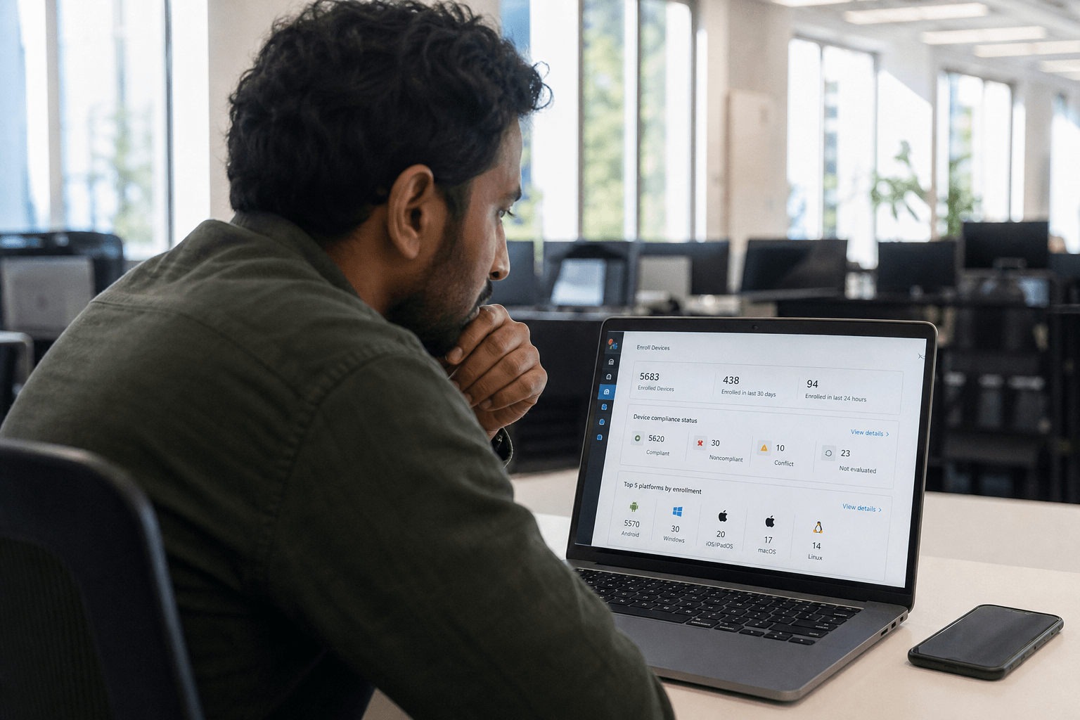 What Is Mobile Device Management and Why Do SMBs Need It? 1 IT professional reviewing MDM dashboard on laptop with smartphone on desk